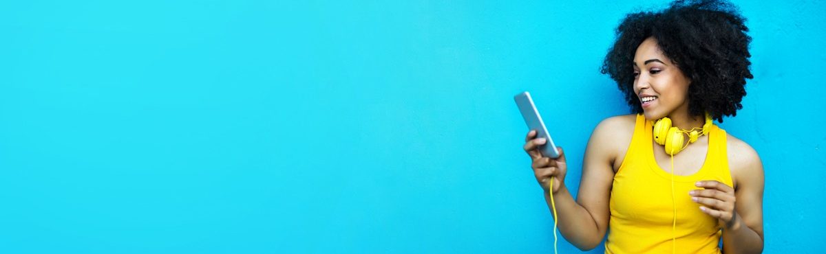 Photo of a young Black woman looking at a mobile phone with headphones draped around her neck, conveying the new 5Cs of marketing